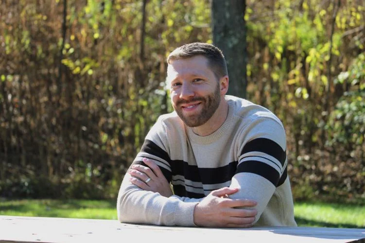 Image of Andrew Akers sat at a bench in a forest for his Standard Journal interview